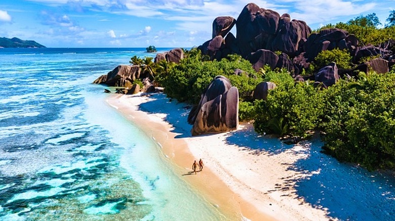 Granite rock formations poke out of the jungle overlooking golden-sand beach with clear blue water
