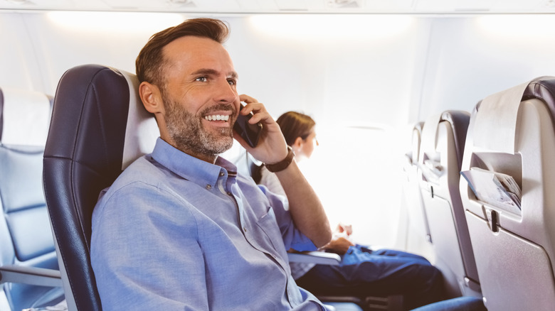 A man talks on a phone on an airplane.