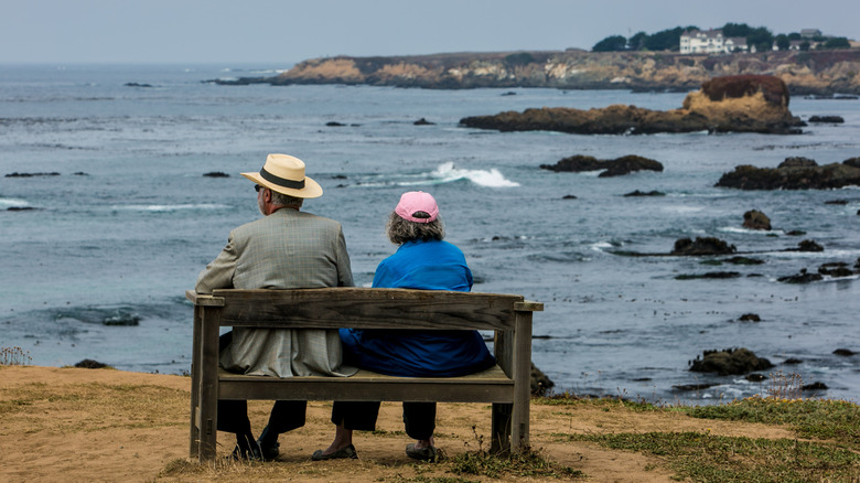 a couple sit on a bench overlooking the Pacific Ocean from the botanical gardens at Mendocino