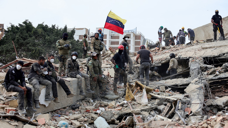Rescuers search for victims at a collapsed building as one raises a Venezuelan flag following a magnitude 7.2 earthquake