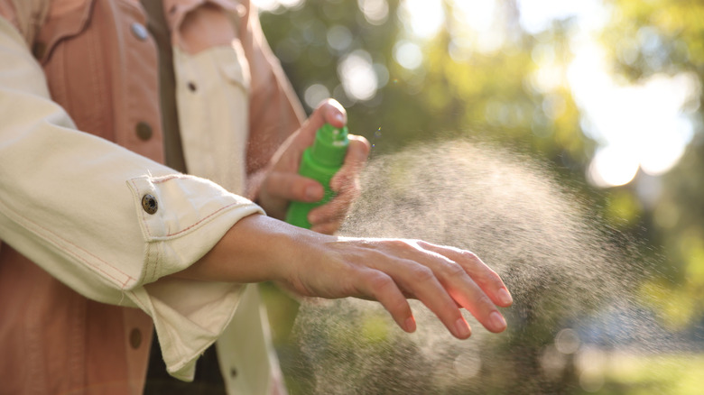 A person putting on bug spray.