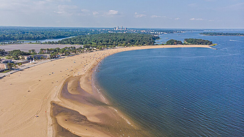 An aerial view of crescent-shaped Orchard Beach, with forest and buildings in the background