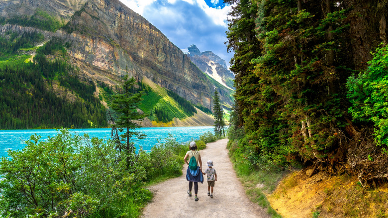 Mother and son walking along a trail on the edge of Lake Louise, with cliffs on one side and forest on the other